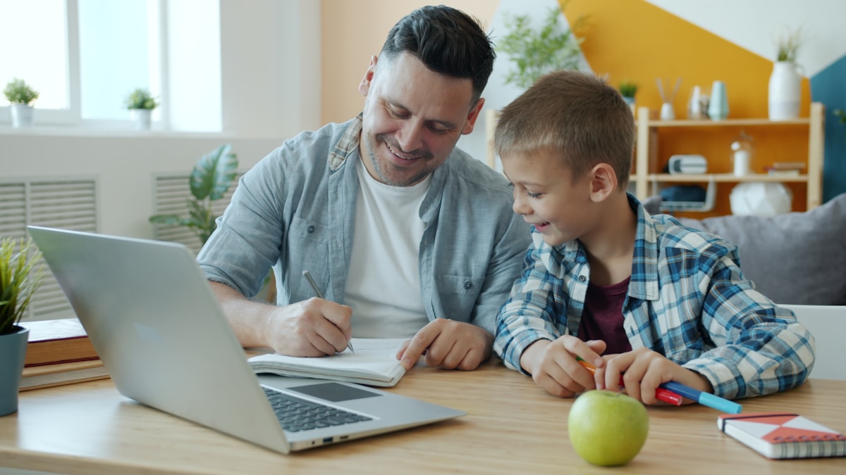 A father and son studying together at a desk with a laptop