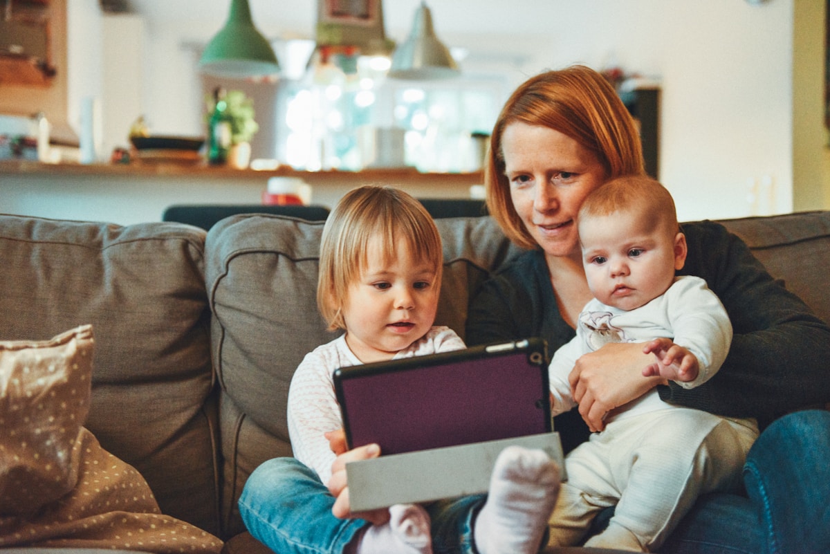 A mother and young children using a tablet together on the couch at home