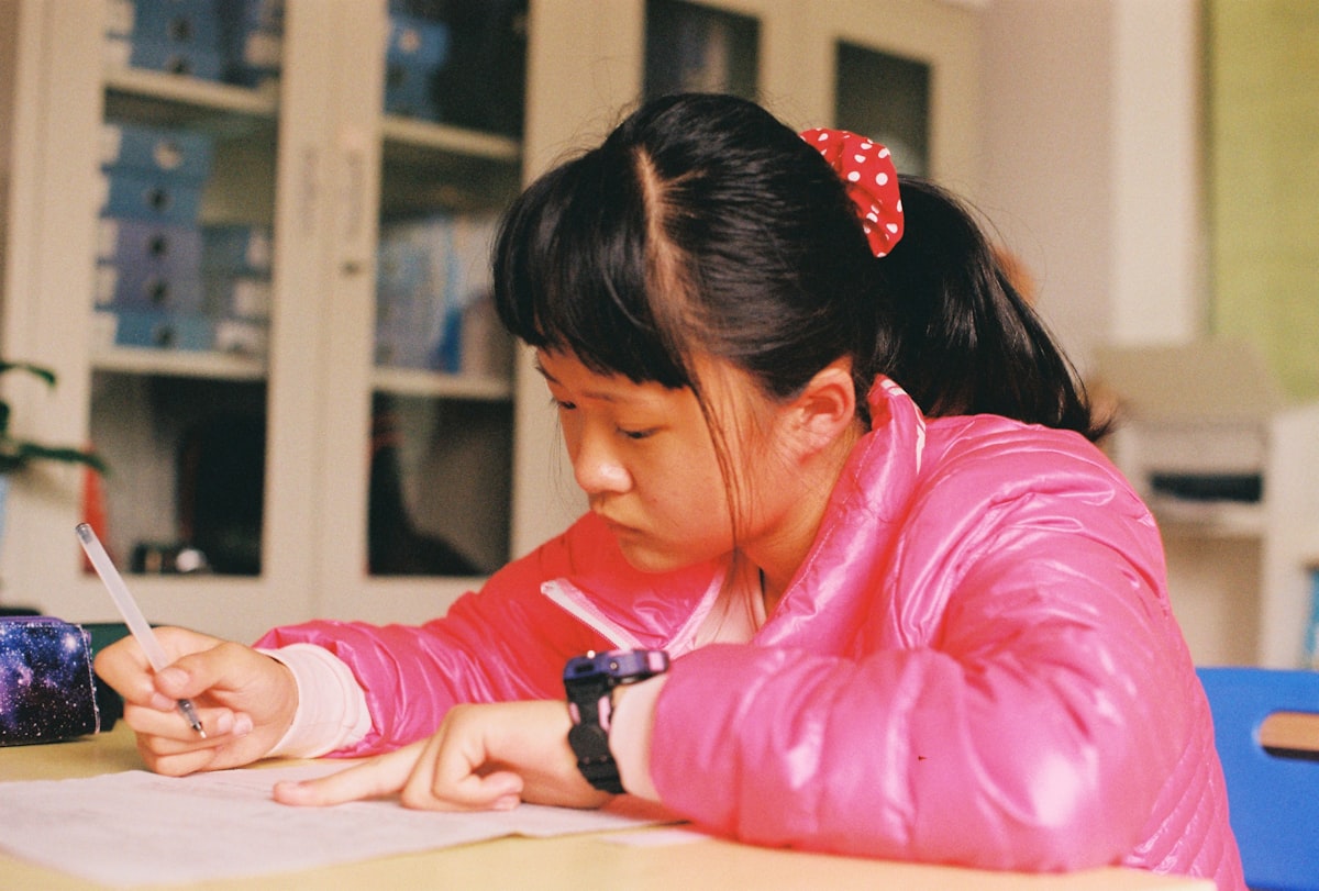 A child practicing writing at a desk with pencils and worksheets