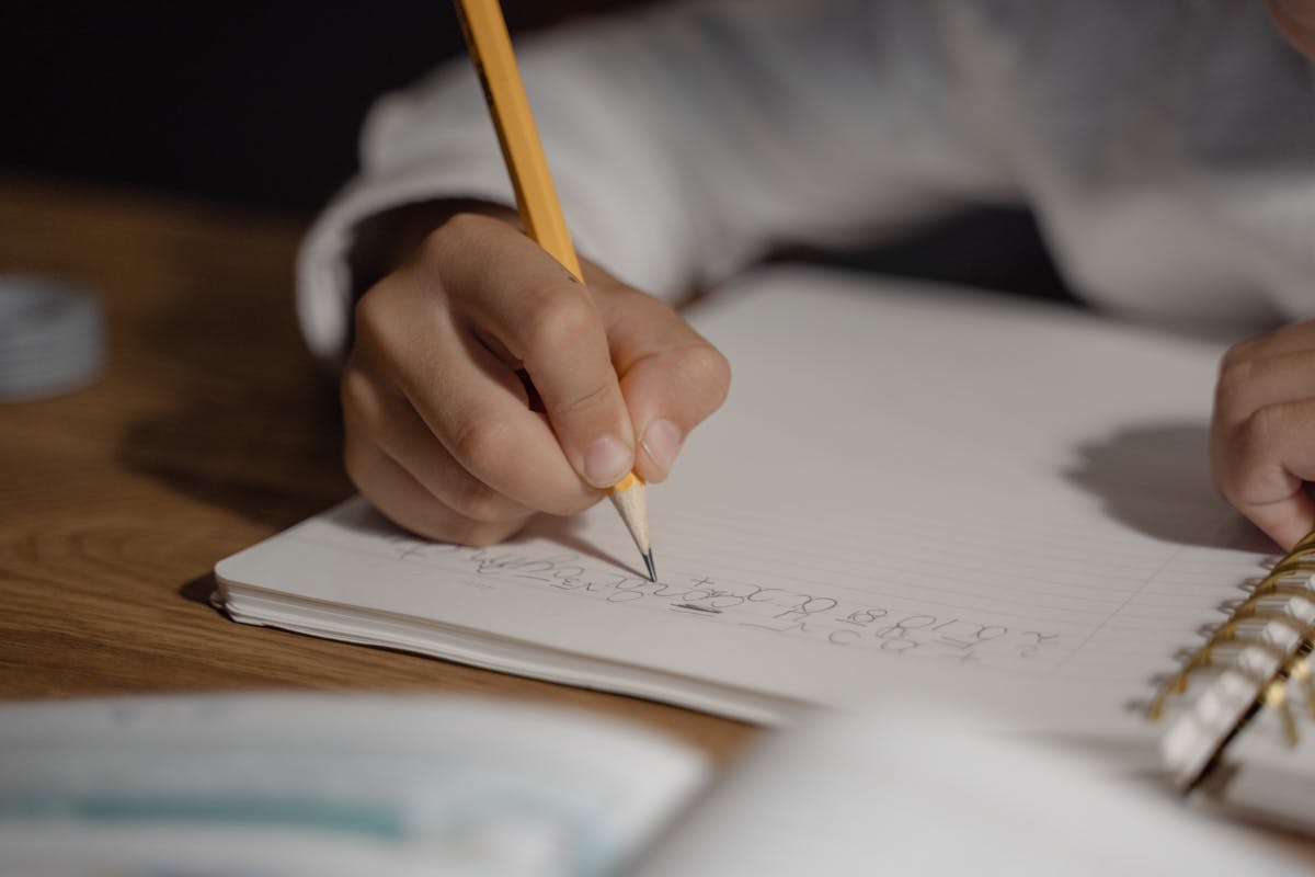 A child writing in a notebook with a pencil