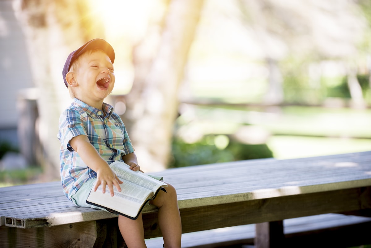 A happy young child laughing while holding a book outdoors