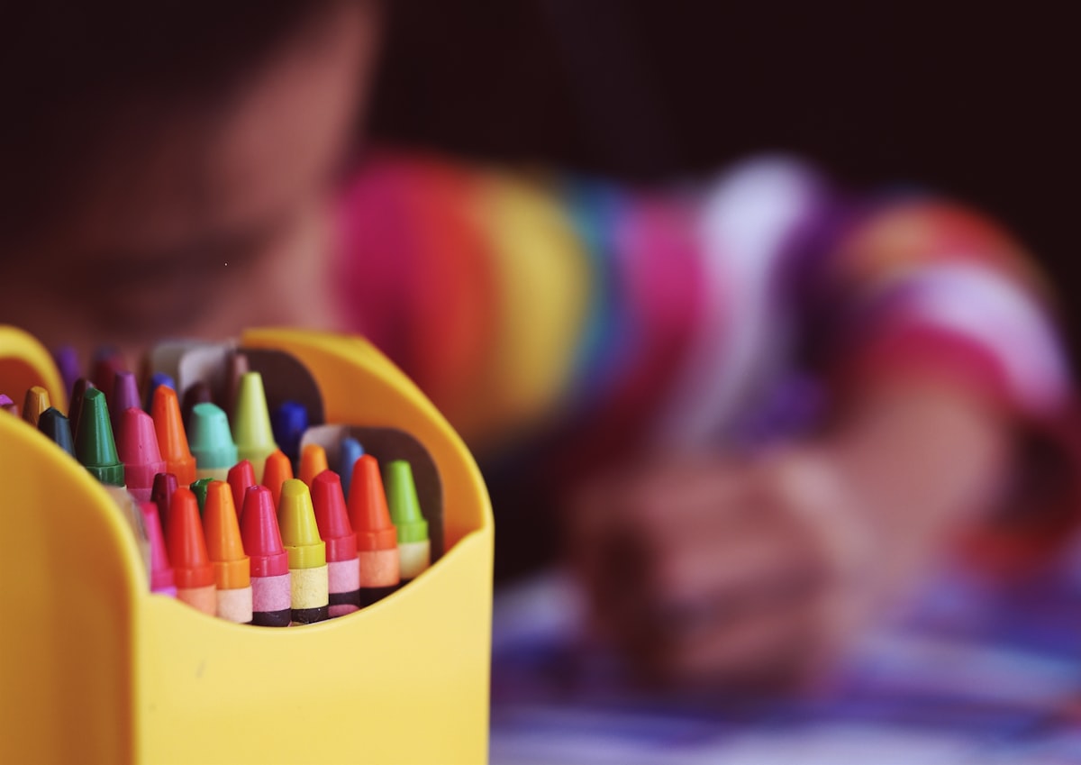 Colorful crayons with a child working on learning activities in the background