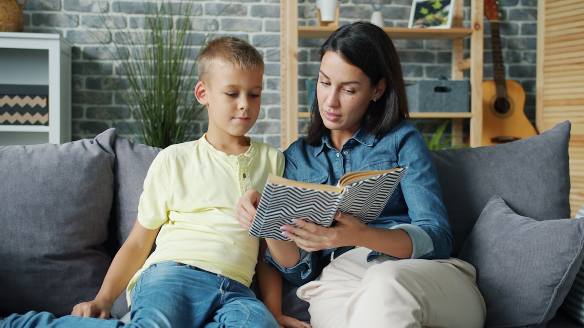 A mother and daughter reading together on a couch at home